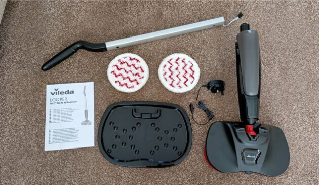 The pieces of the Vileda Looper laid out on a brown carpet. Handle Floor head Four microfibre mop pads Removable water tank Plastic drip tray Charger Instruction manual