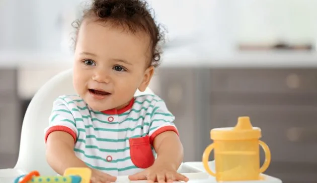 a child in a highchair with a sippy cup