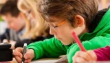 Young boy writing or studying with pen and paper school
