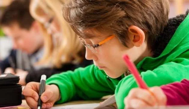 Young boy writing or studying with pen and paper school