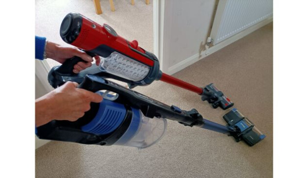 Red Henry Quick cordless vacuum cleaner next to a blue Shark cordless vacuum cleaner