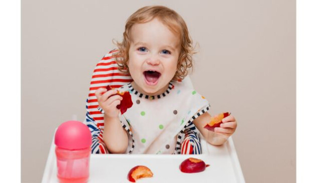 a child in a highchair with a nectraine and sippy cup