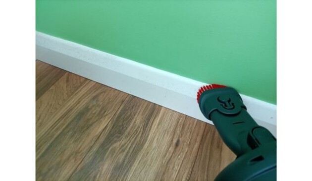 The 2-in-1 Henry Quick combi tool being used to hoover a white skirting board, sitting below a lime green wall and wood-effect floor