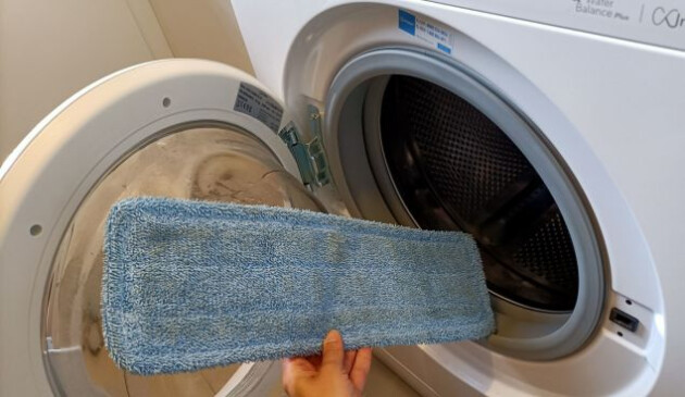 The dirty blue Henry Spray Mop microfibre pad is being placed into the open door of a washing machine.