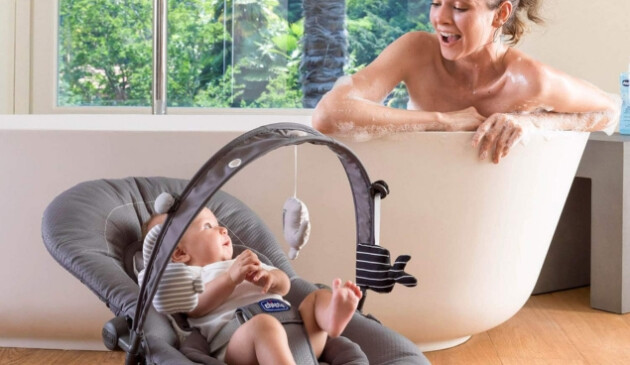 Woman in bath looking at baby in bouncer next to her