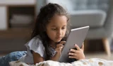 Child lying on floor looking at tablet