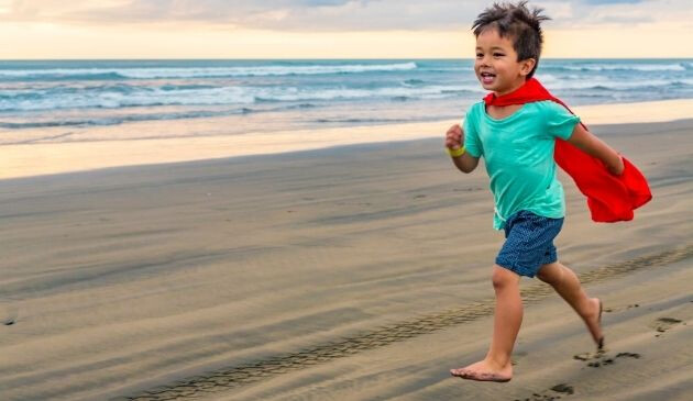 child running on beach wearing red cape