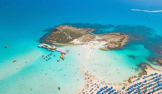 Birds eye-view of turquoise sea with tiny figures of people swimming in the water and tanning on land.