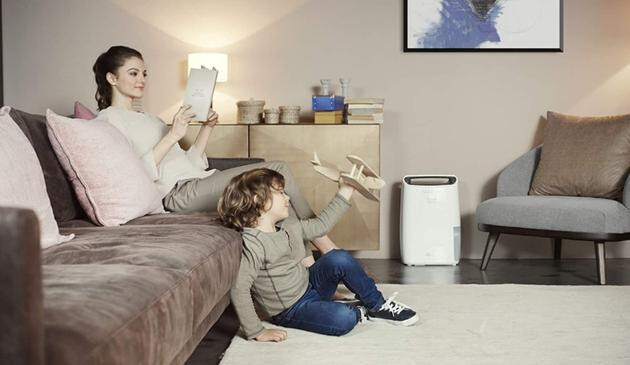 A picture of a boy playing, whilst his Mum relaxes. There is a dehumidifier in the background.