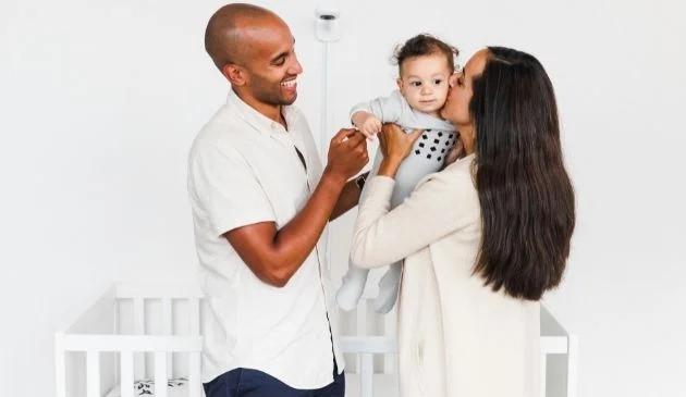 family of three in baby nursery with nanit pro baby monitor in background
