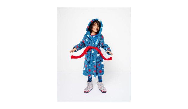 A smiling boy wearing a light blue dressing gown covered with red, white and dark blue stars. The dressing gown has a hood and a red tie around the waist.