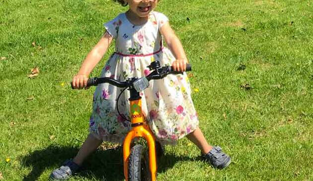 A girl in a dress riding a Frog Tadpole balance bike