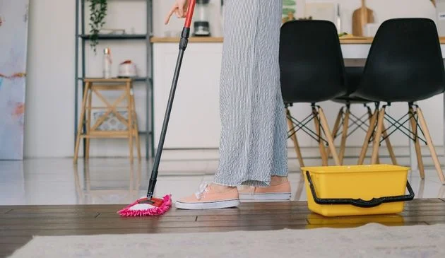 A woman cleaning a wooden floor with a mop