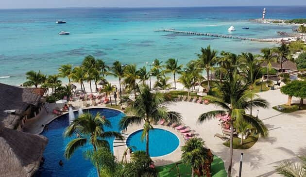 Blue ocean surrounded by palm trees and two small, circular swimming pools with a swim-up bar