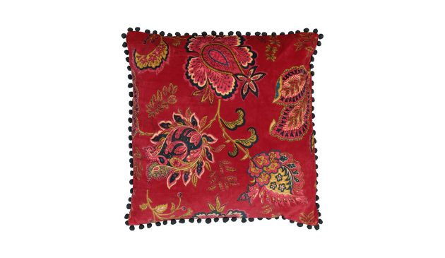 A red cushion with a pomegranate pattern and pom pom trim