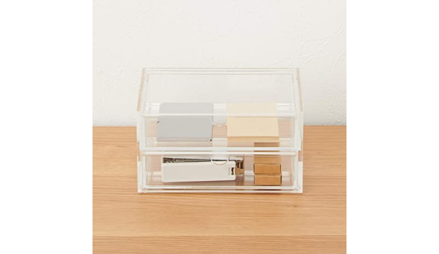 a transparent storage box on a wooden table, filled with stationery