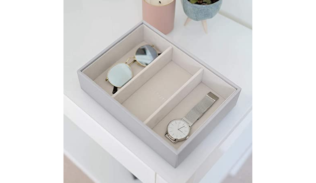 a jewellery box with sunglasses and a watch inside, on a tidy dressing table