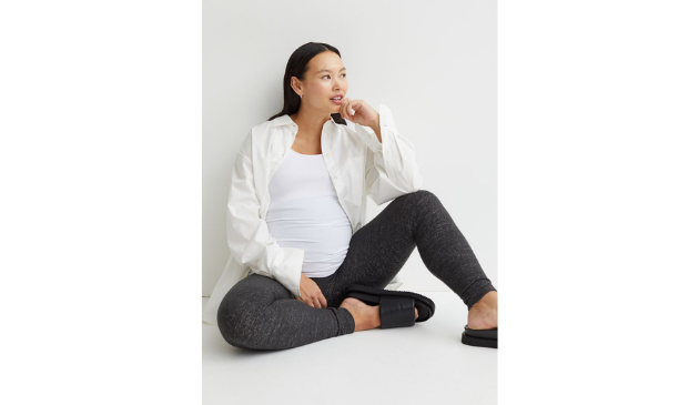 a woman wearing a loose white shirt and leggings, sitting on the floor