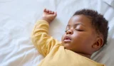 A baby sleeps on his back with his right arm up