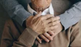 A daughter wraps her arms around her elderly father's shoulders