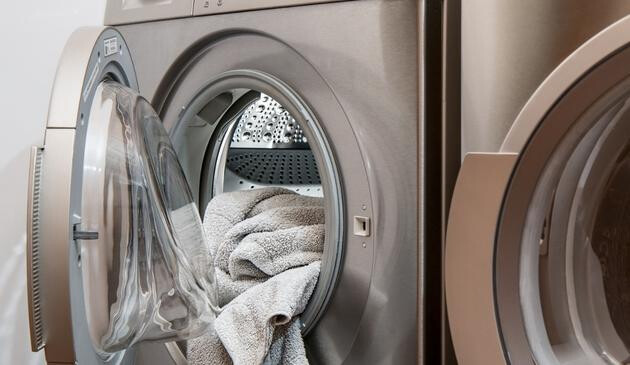 A picture of a grey tumble dryer and washing machine next to each other with a towel hanging out.