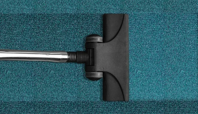 A black vacuum cleaner head on a teal carpet