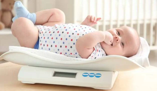 Small baby on scales with fingers in mouth