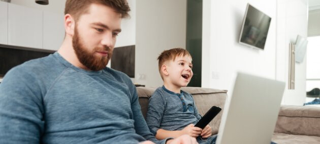 Dad on laptop while child enjoys TV